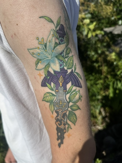 Tatouage coloré d'une dague entourée de végétaux
